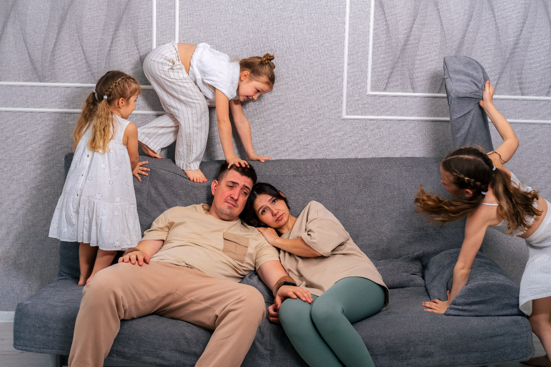 Pareja agotada en el sillón con sus hijos jugando alrededor
