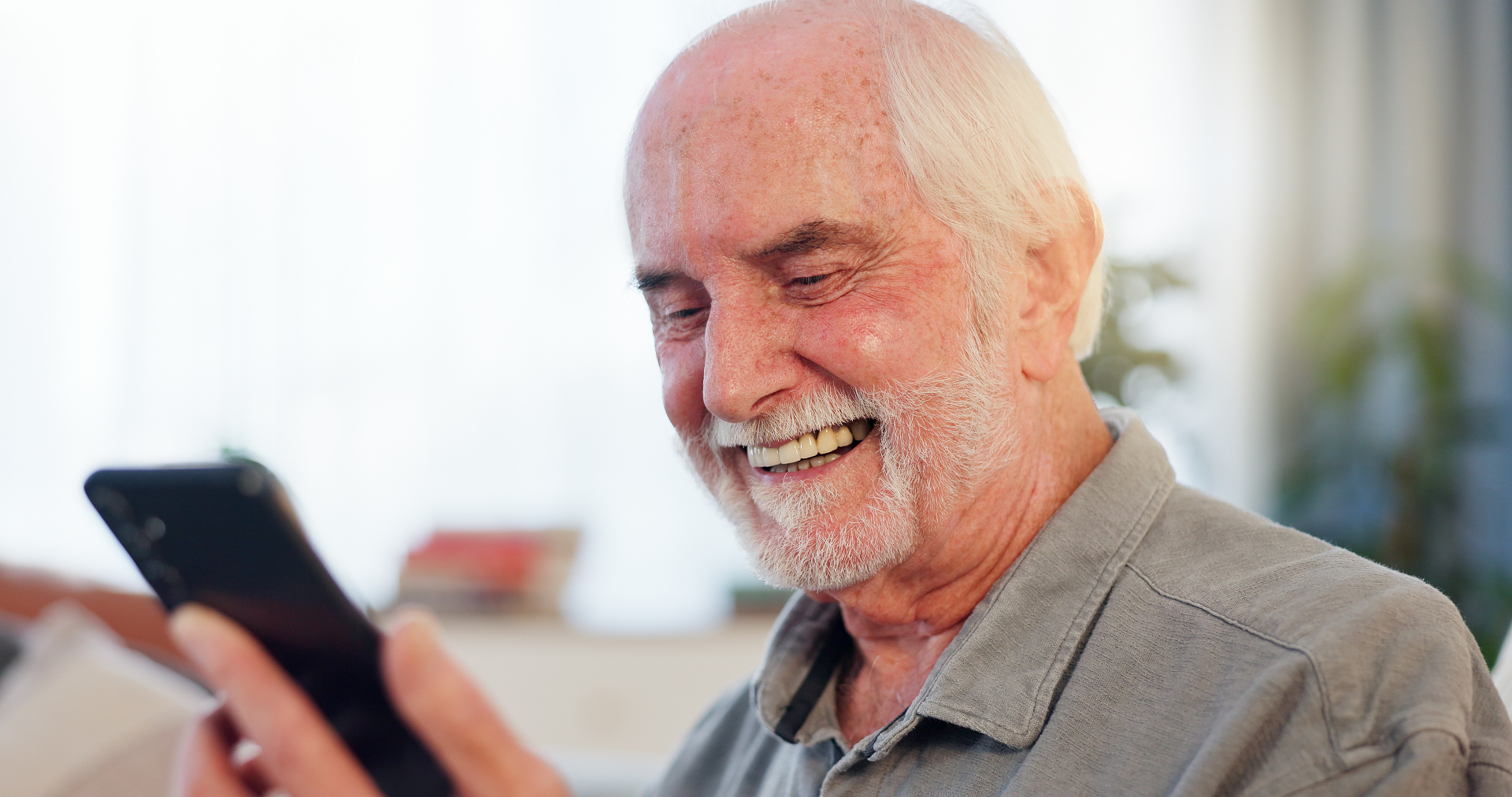 Adulto mayor riendo mientras usa su teléfono